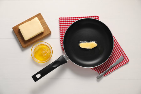 Melting butter in frying pan and knife on white wooden table, flat layの写真素材