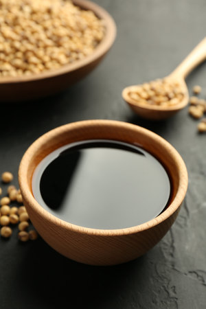 Tasty soy sauce in bowl and soybeans on black table, closeupの写真素材