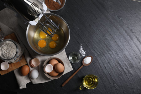 Making dough. Raw eggs in bowl of stand mixer and ingredients on black table, flat lay with space for textの写真素材