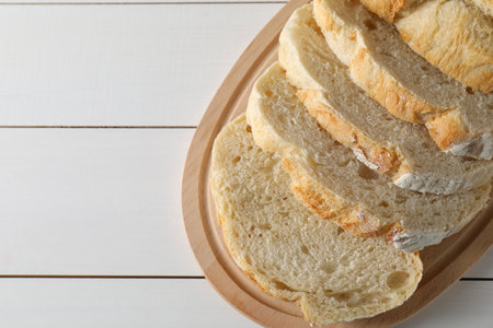 Freshly baked cut sourdough bread on white wooden table, top view. Space for text