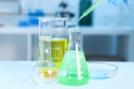 Laboratory analysis. Woman dripping liquid into flask at white table indoors, closeupの写真素材