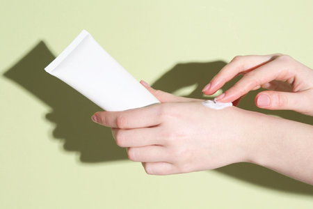 Woman with tube applying cream on her hand against green background, closeupの写真素材