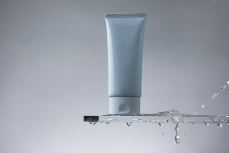 Moisturizing cream in tube on glass with water drops against gray background