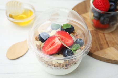 Tasty granola with berries, yogurt and almond flakes in plastic cup on white table, closeupの写真素材