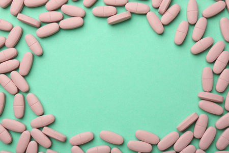 Frame made of pink vitamin capsules on turquoise background, top view. Space for textの写真素材