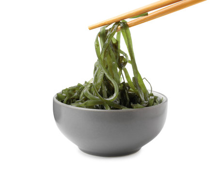 Taking tasty seaweed salad from bowl on white backgroundの写真素材