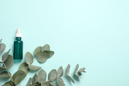 Aromatherapy product. Bottle of essential oil and eucalyptus branches on light blue background, flat lay. Space for textの写真素材