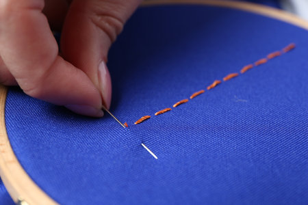 Woman with sewing needle and thread embroidering on cloth, closeup
