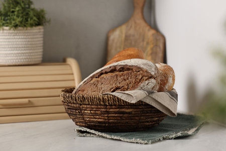 Wicker bread basket with freshly baked loaves on white marble table in kitchenの写真素材