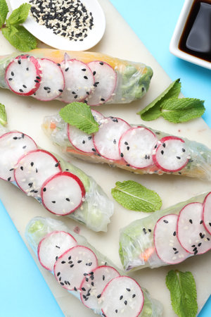 Delicious spring rolls, mint, sesame and soy sauce on light blue background, top view