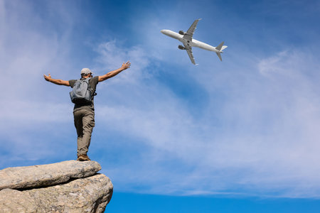 Man on cliff looking at airplane flying in skyの写真素材
