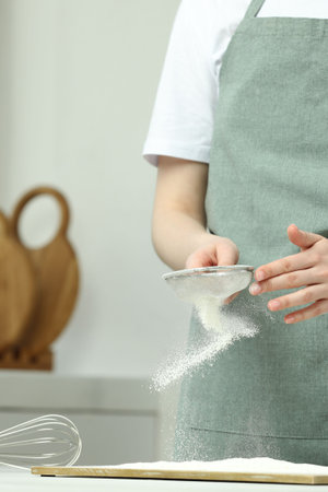 Woman sieving flour at table in kitchen, closeup. Space for textの写真素材