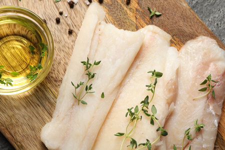 Raw cod fish, microgreens, oil and spices on gray textured table, top view