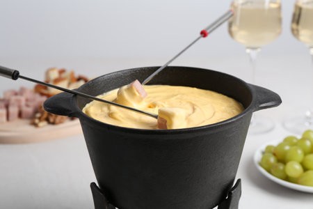 Dipping ham into fondue pot with tasty melted cheese at white table, closeupの写真素材
