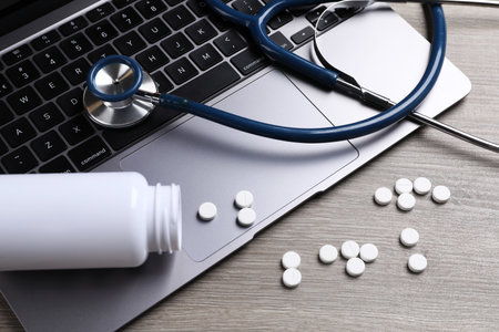 Laptop, stethoscope, pills and bottle on wooden table, closeupの写真素材