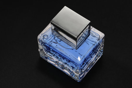 Blue men's perfume in bottle on black background, closeup