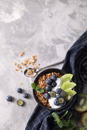 Tasty granola with yogurt, blueberries and kiwi in bowl on gray textured table, flat lay. Space for textの写真素材