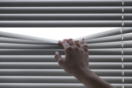 Woman separating slats of white blinds indoors, closeupの写真素材