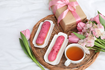 Tasty breakfast. Delicious eclairs, tea, flowers and gift box on bedの写真素材