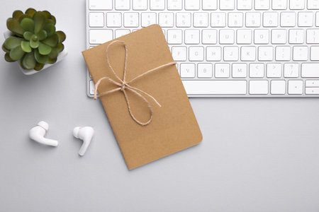 Office workplace. Keyboard, houseplant, earphones and notebook on light gray table, flat layの写真素材