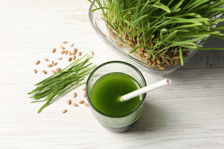 Wheat grass drink in glass, seeds and fresh green sprouts on white wooden table, flat layの写真素材