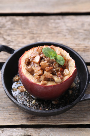 Tasty baked apple with nuts, honey and mint in baking dish on wooden table, closeupの写真素材