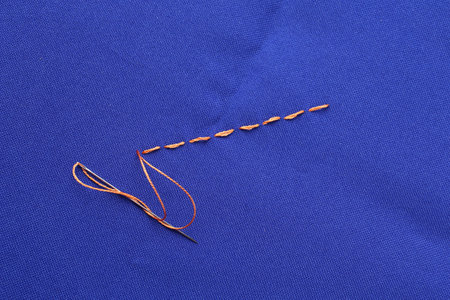 Sewing needle with thread and stitches on blue cloth, top view