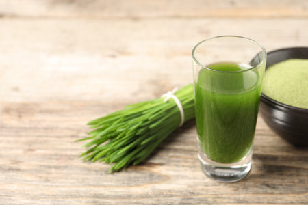 Wheat grass drink in shot glass and fresh green sprouts on wooden table, closeup. Space for textの写真素材