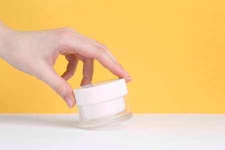 Woman with jar of cream on yellow background, closeupの写真素材