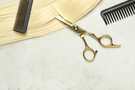 Professional hairdresser scissors and comb with blonde hair strand on gray table, top view. Space for textの写真素材
