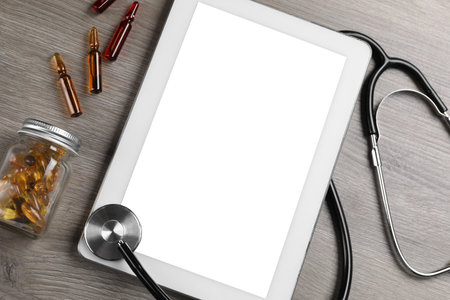 Modern tablet, stethoscope, ampoules and bottle with pills on wooden table, flat layの写真素材