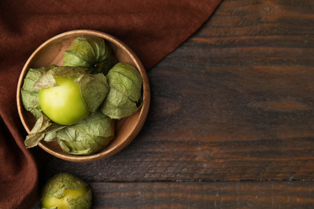Fresh green tomatillos with husk in bowl on wooden table, top view. Space for textの写真素材