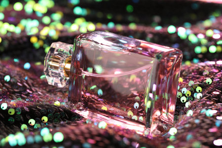 Luxury perfume in bottle on fabric with colorful sequins, closeup