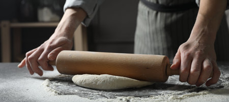 Woman rolling pizza dough with pin at table, closeup