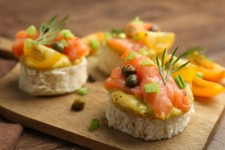 Tasty canapes with salmon served on wooden table, closeup