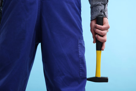 Professional repairman holding hammer on light blue background, closeupの写真素材