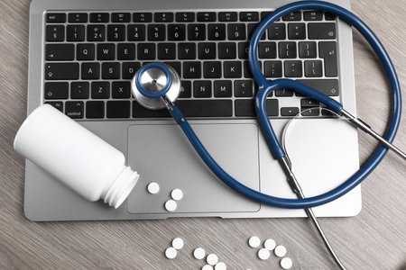 Laptop, stethoscope, pills and bottle on wooden table, flat layの写真素材