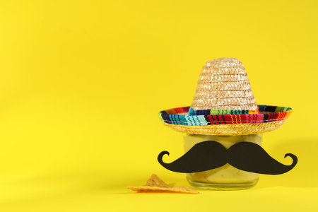 Delicious guacamole, nachos chip, Mexican sombrero hat and fake mustache on yellow background. Space for textの写真素材