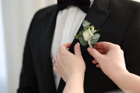 Bride putting boutonniere on her groom's jacket against light background, closeup. Wedding accessoryの写真素材