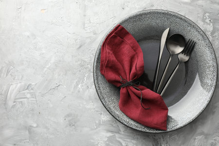 Stylish setting with cutlery, napkin and plate on gray textured table, top view. Space for textの写真素材