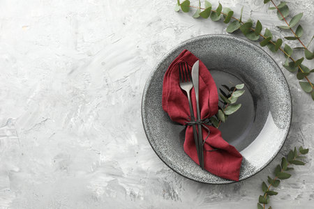 Stylish setting with cutlery, napkin, eucalyptus branches and plate on gray textured table, top view. Space for textの写真素材