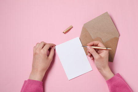 Woman writing letter on pink table, top view. Space for textの写真素材