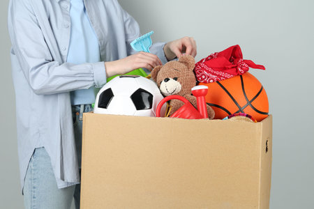 Woman with box of unwanted stuff on gray background, closeup