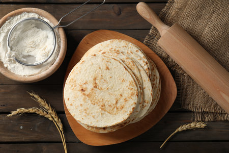 Many tasty homemade tortillas and rolling pin on wooden table, top viewの写真素材
