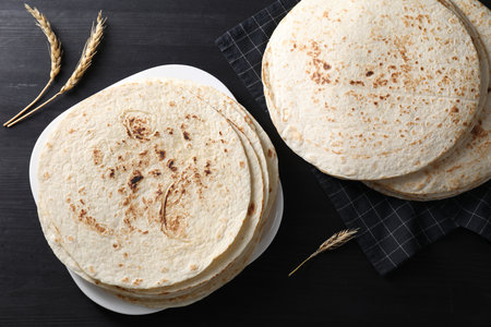 Many tasty homemade tortillas on black wooden table, top view