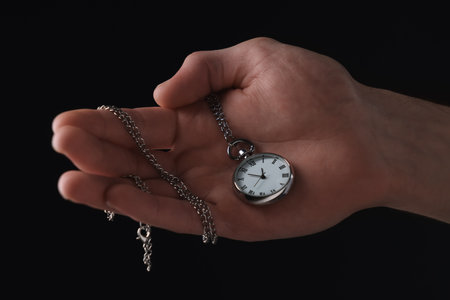 Man holding chain with elegant pocket watch on black background, closeupの写真素材