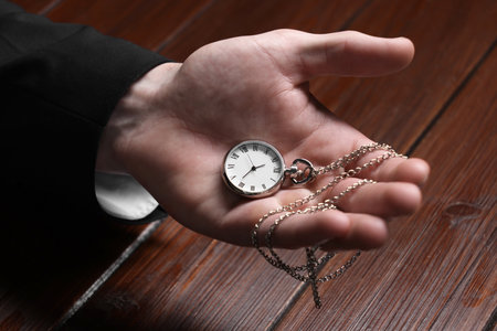 Man holding chain with elegant pocket watch at wooden table, closeupの写真素材