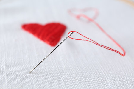 Embroidered red hearts and needle on white cloth, closeupの写真素材