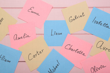 Paper stickers with different names on pink wooden background, flat lay. Choosing baby's name