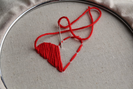 Embroidered red heart and needle on light cloth, closeupの写真素材